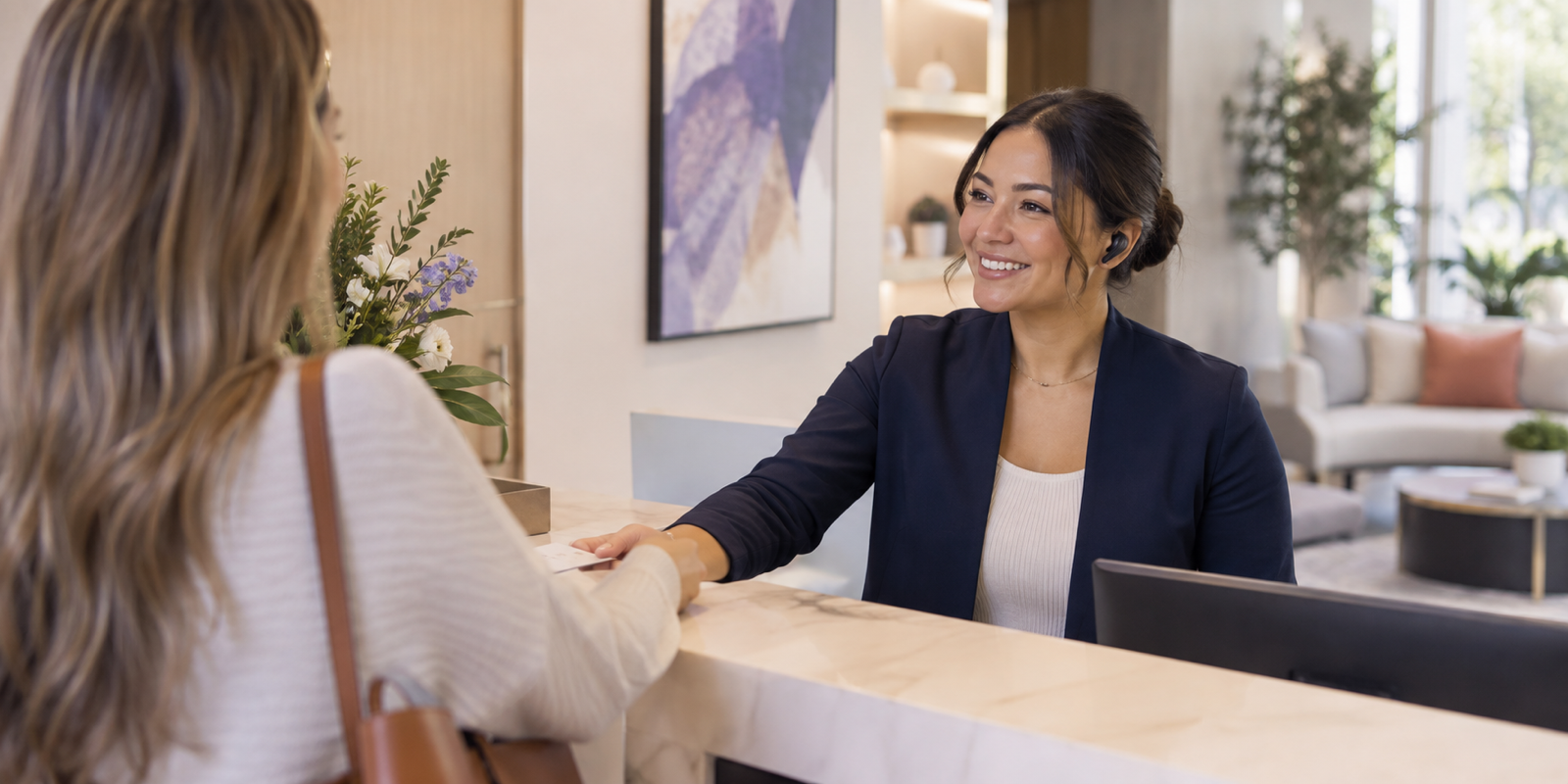 A front desk professional welcoming a visitor while handling calls through a wireless earpiece